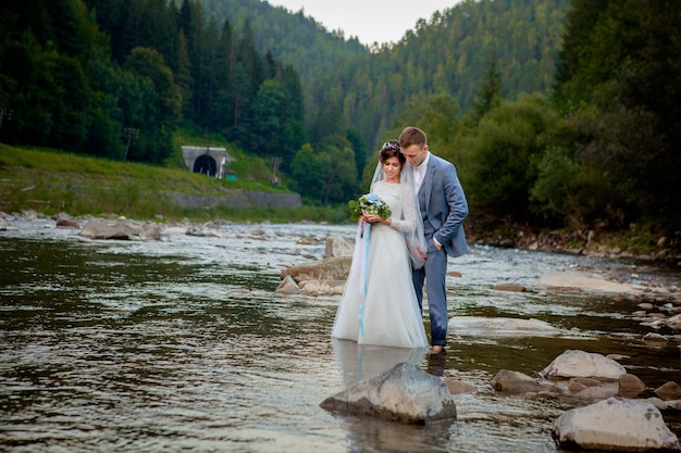 Recién casados felices de pie y sonriendo en el río. Luna de miel, foto para el día de San Valentín.