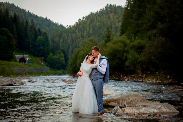 Recién casados felices de pie y sonriendo en el río.