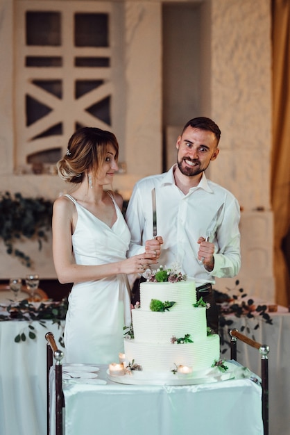 Recién casados felizmente cortan, ríen y prueban el pastel de bodas