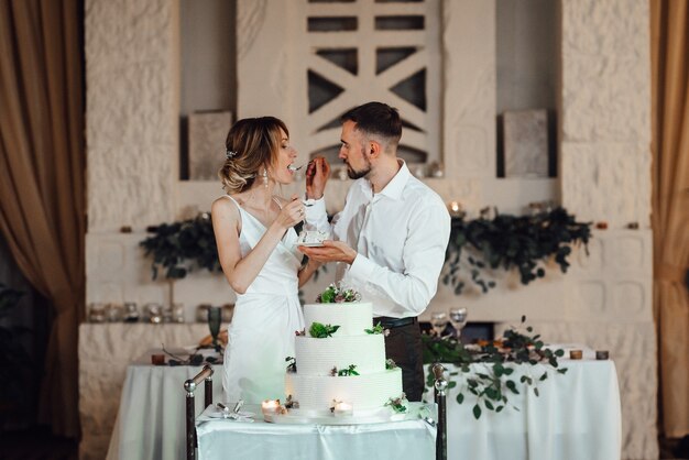 Recién casados felizmente cortan, ríen y prueban el pastel de bodas