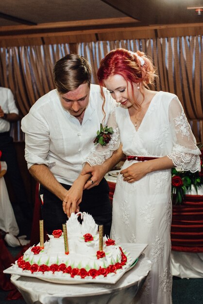 Recién casados felizmente cortan, ríen y prueban el pastel de bodas