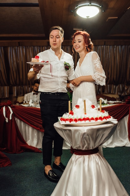 Recién casados felizmente cortan, ríen y prueban el pastel de bodas