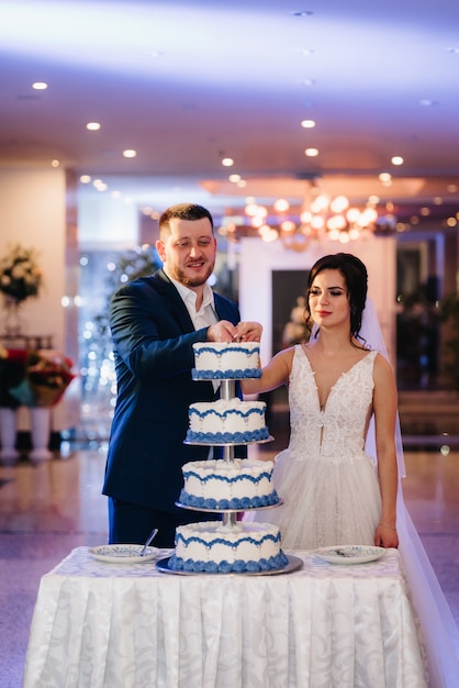 Recién casados felizmente cortan, ríen y prueban el pastel de bodas
