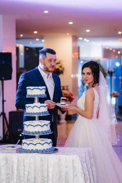 Recién casados felizmente cortan, ríen y prueban el pastel de bodas