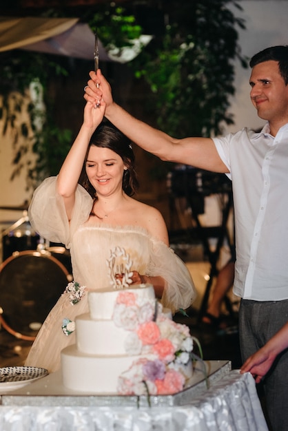 Recién casados felizmente cortan, ríen y prueban el pastel de bodas