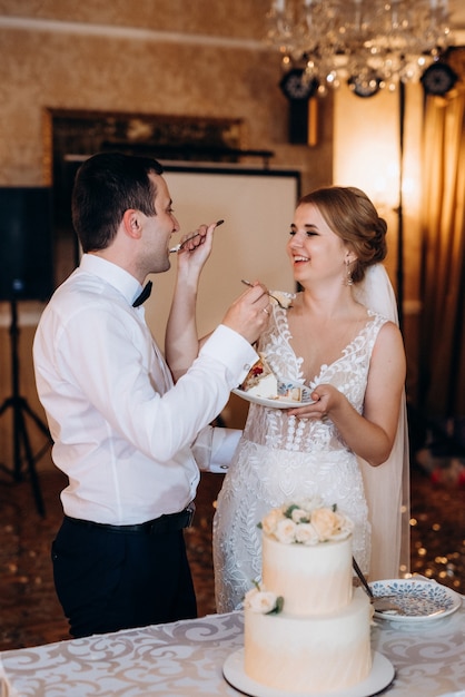 Recién casados felizmente cortan, ríen y prueban el pastel de bodas