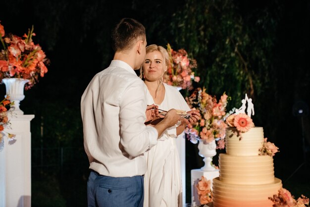 Recién casados felizmente cortan, ríen y prueban el pastel de bodas