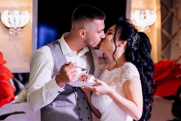 Recién casados felizmente cortan, ríen y prueban el pastel de bodas