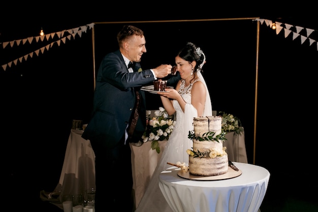 Recién casados felizmente cortan, ríen y prueban el pastel de bodas