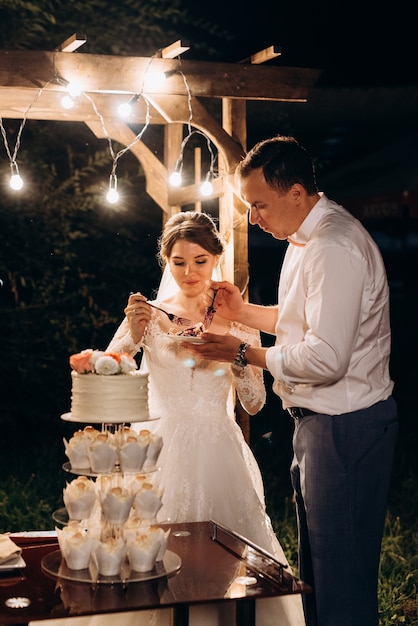 Recién casados felizmente cortan, ríen y prueban el pastel de bodas