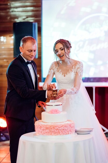 Recién casados felizmente cortan, ríen y prueban el pastel de bodas