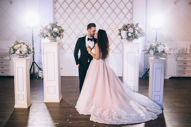 Recién casados muy hermosos y felices se paran cerca de un arco de boda bellamente decorado en su ceremonia de boda