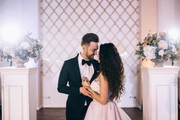 Recién casados muy hermosos y felices se paran cerca de un arco de boda bellamente decorado en su ceremonia de boda