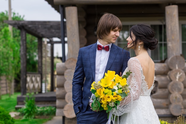 Recién casados posando cerca de lujosa mansión de madera en la ceremonia de la boda