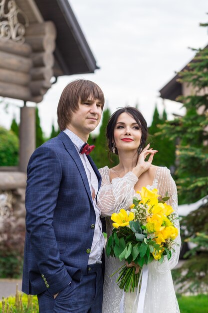 Recién casados posando cerca de lujosa mansión de madera en la ceremonia de la boda