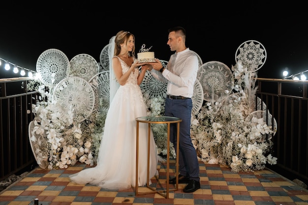 Los recién casados se ríen felizmente y prueban el pastel de bodas