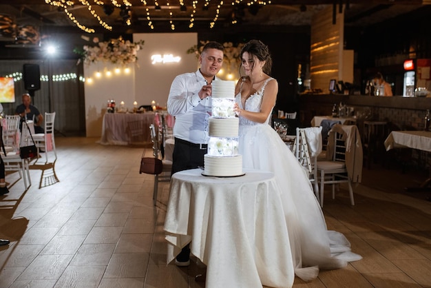 Los recién casados se ríen felizmente y prueban el pastel de bodas