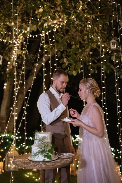 Los recién casados se ríen felizmente y prueban el pastel de bodas