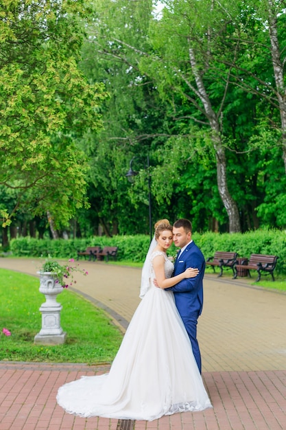 Recién casados en ropa festiva abrazándose en un hermoso parque. Parque con linternas y bancos.