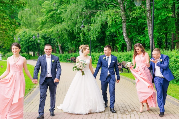 Los recién casados y sus amigos se toman de la mano y caminan por el parque.