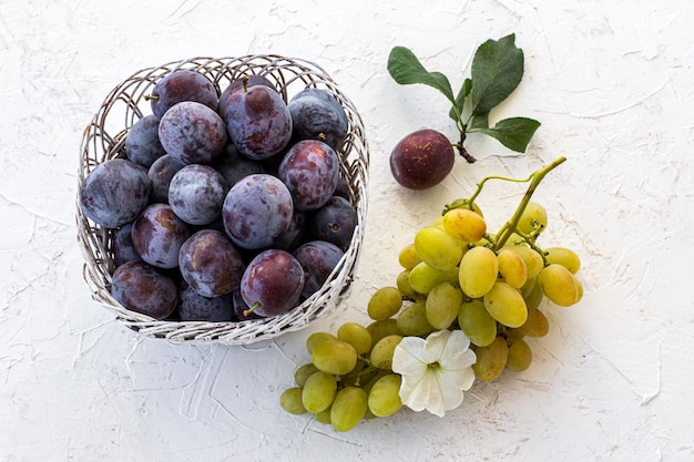 Recién cogido ciruelas maduras en cesta de mimbre y un racimo de uvas blancas maduras
