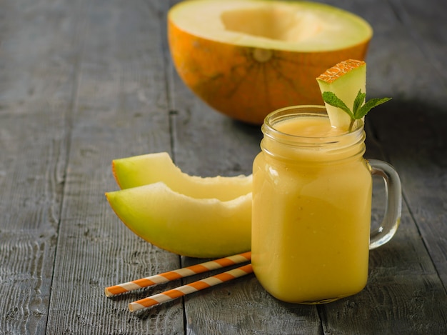 Recién hecho melón, naranja y banansmoothies y dos tubos de cóctel en la mesa de madera oscura.