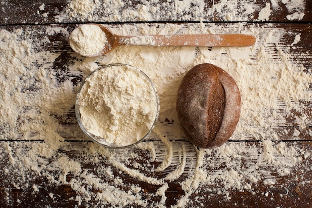 Recién horneado, un bol de pan sabroso con harina y una cuchara de madera están sobre la mesa espolvoreados con harina de trigo