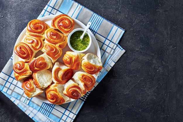 Recién horneado Hot Pull Apart rolls Bollos de cena de levadura casera en un plato blanco con salsa de ajo y perejil en un tazón sobre una mesa de hormigón vista horizontal desde arriba espacio de copia plana