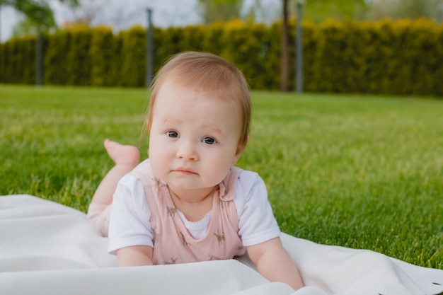 Recién nacido niña lactante acostada sobre una tela escocesa blanca sobre la hierba en un parque