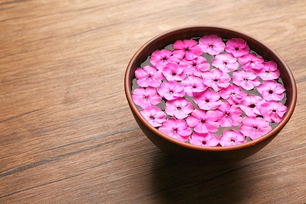 Recipiente con agua y flores de color rosa sobre fondo de madera