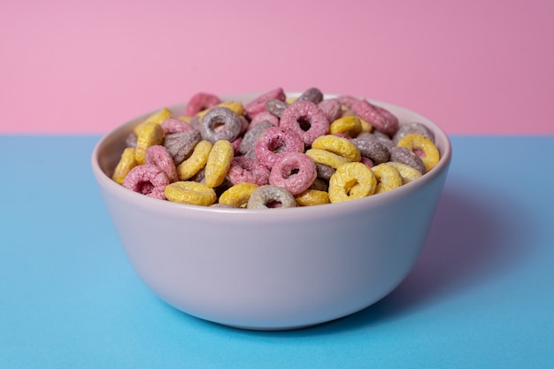 Recipiente aislado de cereales y malvaviscos mixtos sobre un fondo azul y rosa