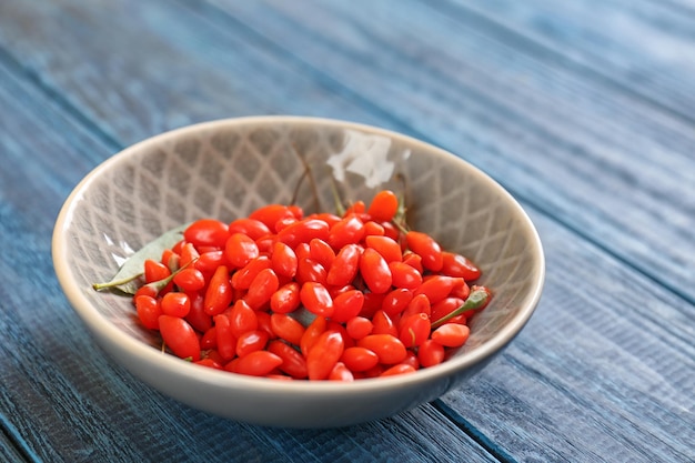 Recipiente con bayas de goji frescas sobre mesa de madera