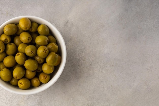 Foto recipiente blanco lleno de jugosas aceitunas verdes sobre un fondo claro