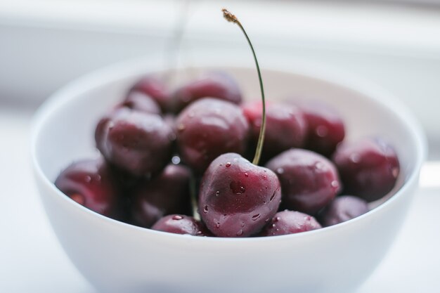 Recipiente blanco parcialmente borrosa con cerezas rojas maduras, sobre superficie blanca