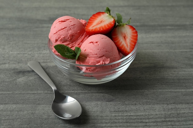 Recipiente con bolas de helado de fresa en mesa con textura gris