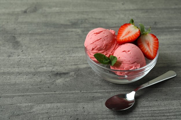 Recipiente con bolas de helado de fresa en mesa con textura gris