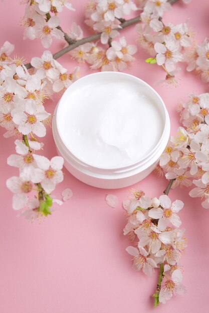 Recipiente con crema para el cuidado del cuerpo y la piel sobre un fondo rosa con cereza floreciente Cuidado de la piel facial cosmético y spa Concepto de tratamiento natural