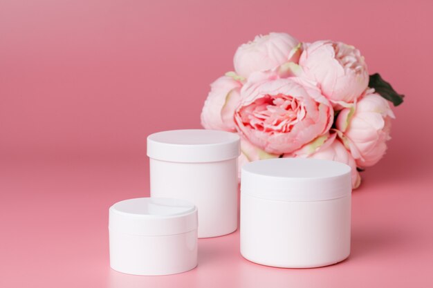 Foto recipiente de creme cosmético e flores cor de rosa na queixa-de-rosa