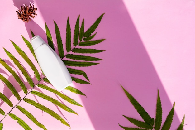 Recipiente de frasco cosmético branco com folha de palmeira e flor de pinheiro em fundo de papel rosa. Conceito de produto de beleza orgânico natural, estilo minimalista de verão