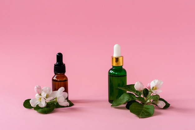 Recipiente de garrafa de skincare natural com folha verde, ingredientes de flores em fundo rosa. Remédio caseiro e conceito de produto de beleza.