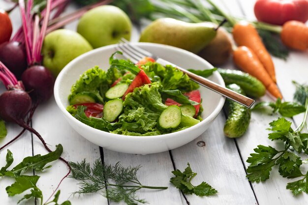 Recipiente con ensalada fresca de verano e ingredientes en la mesa de madera blanca, comida sana