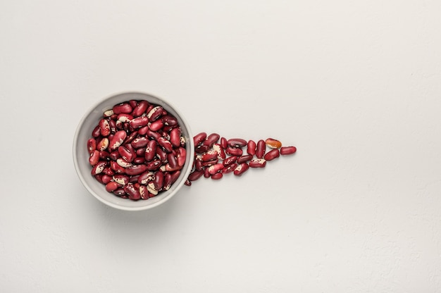 Recipiente con frijoles rojos sobre una superficie de textura ligera junto al grano se vierte en forma de un