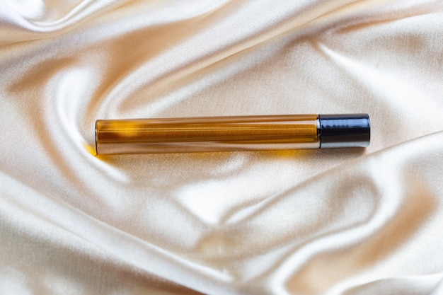 Un recipiente para guardar cosméticos hecho de vidrio oscuro se encuentra en los pliegues de una tela de satén de seda
