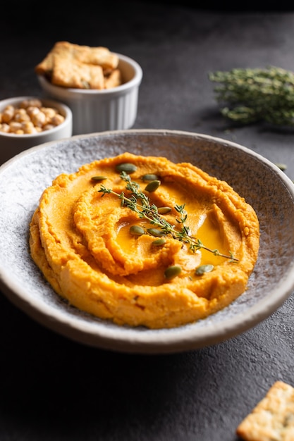 Recipiente con hummus de calabaza, delicioso aperitivo decorado con verduras y especias