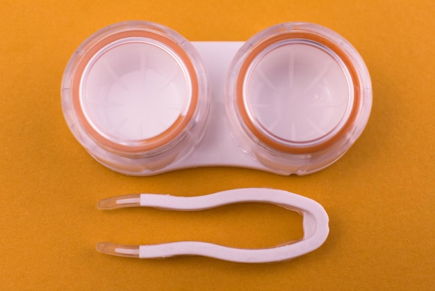 Recipiente laranja para lentes de contato e pinças em um fundo laranja Closeup