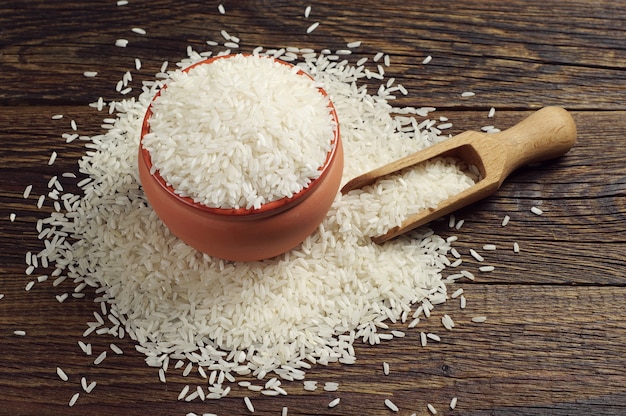 Recipiente lleno de arroz blanco y cuchara en la mesa de madera oscura.