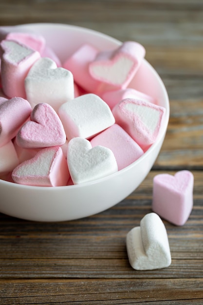 Recipiente con malvaviscos en forma de corazón rosas y blancos sobre un fondo de madera cerrado