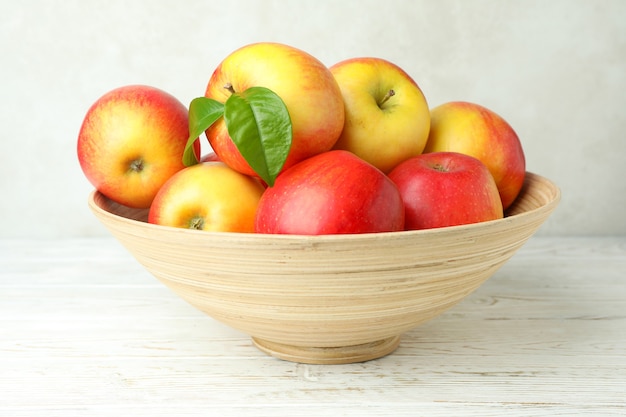 Recipiente con manzanas rojas sobre la mesa de madera blanca