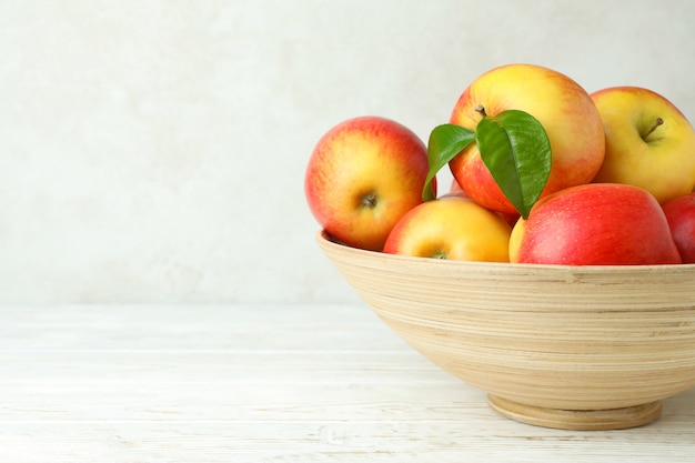 Recipiente con manzanas rojas sobre la mesa de madera blanca