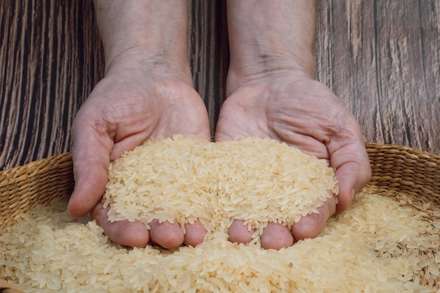 Recipiente marrón lleno de granos de arroz blanco secos Manos llenas de granos de arroz blanco frescos